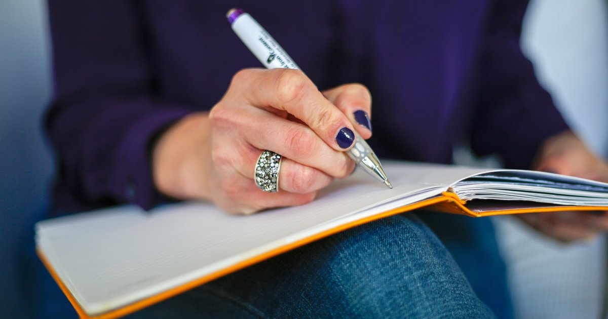 Person writing in a notebook with a pen